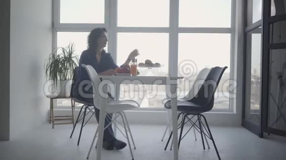 镜头接近孤独的白种人女人拿着羊角面包看着窗外的室内富有的成年人视频的预览图