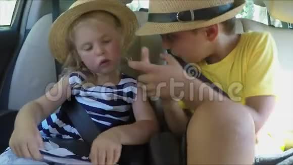 小男孩和一个戴帽子的金发女孩正坐在车后座上视频的预览图