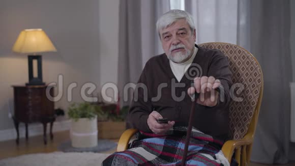 高加索人的肖像与步行拐杖切换通道与遥控器老年男性退休人员休息视频的预览图