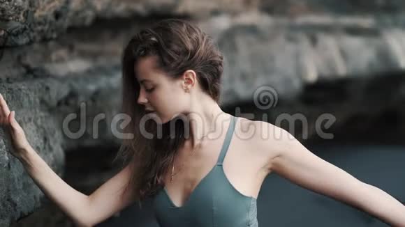 在悬崖附近的黑沙滩上做伸展运动的女人视频的预览图