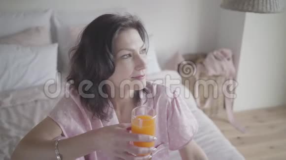 一位美丽的黑发白种人女人喝着橙汁微笑着有魅力的年轻女士画像视频的预览图
