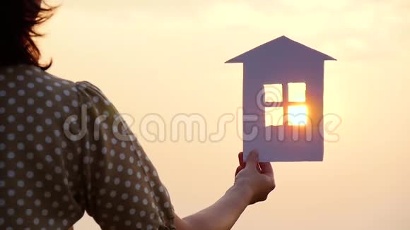 一个女孩手里拿着纸房子模型的剪影日落时太阳的光线穿过视频的预览图