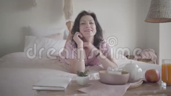美丽的成年白种人女人早上躺在床上微笑的肖像布鲁内特自信的女士视频的预览图