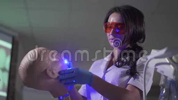 集中年轻的深色头发的女人使用牙科模特上的固化灯忙碌的高加索口腔医生的画像视频的预览图