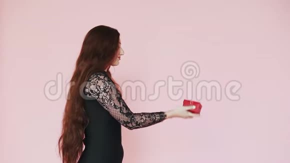 年轻的白种人红发女孩在粉红色的背景下在你的手心里拿出一份礼物慢动作三月八日的主题视频的预览图