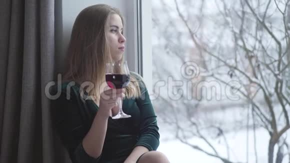 体贴的年轻白种人女人望着窗外喝着酒杯里的红酒孤独美丽的女孩视频的预览图