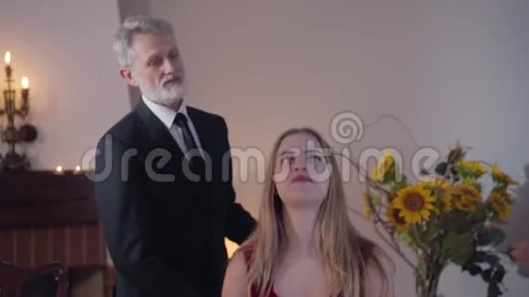 优雅的中年白人男子帮助美丽的女人坐在椅子上穿红色裙子的漂亮姑娘视频的预览图