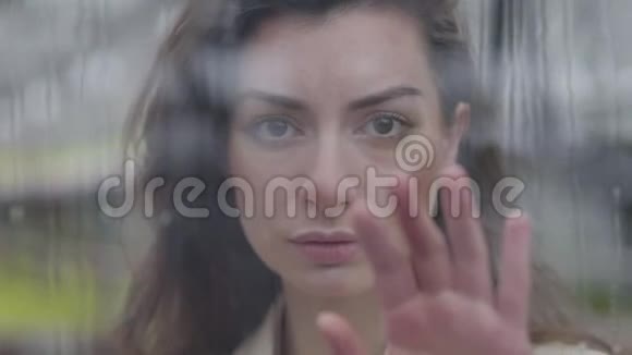 一位年轻的高加索女人站在玻璃后面用手触摸窗户美丽的黑发肖像视频的预览图