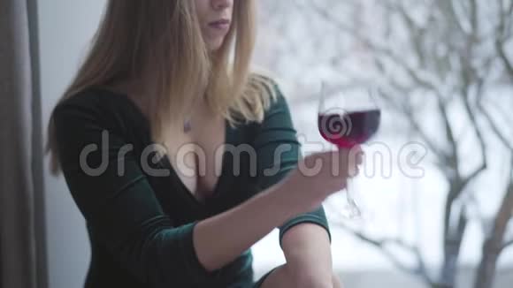 无法辨认的年轻女子穿着优雅的衣服在室内喝红酒白种人女士坐在窗台上思考视频的预览图