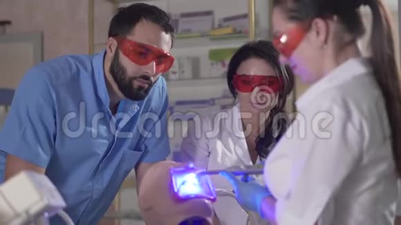 三名专业牙科助理使用人体模型上的固化灯中东男子和高加索妇女视频的预览图