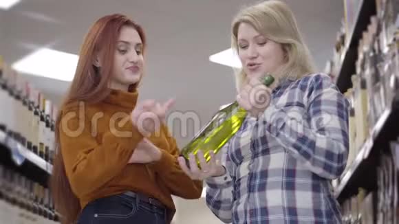 美丽的白种人女孩思考超市葡萄酒选择的肖像金发女郎和红发女郎视频的预览图