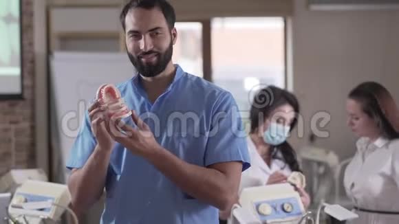正面的中东男牙科医生在镜头前微笑的肖像手里拿着牙齿同事在镜头前视频的预览图