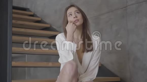 白种人年轻女子坐在室内楼梯上做梦的肖像快乐美丽的女孩思考视频的预览图