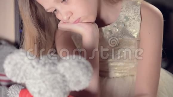 一个小悲伤失望的女孩坐在人造壁炉旁在柔软的玩具旁边感到悲伤被宠坏的概念视频的预览图