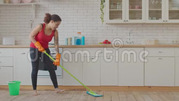 积极的混血妇女拖厨房地板视频的预览图