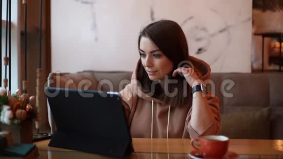 一位穿着休闲服的年轻美女正在一家舒适的咖啡馆使用数码平板电脑视频的预览图
