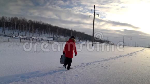 一个穿着红色夹克背着背包的男旅行者在冬天的街上沿着雪路走视频的预览图