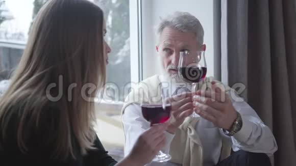 英俊的年长男人手里拿着酒杯和年轻的黑发白种人女人在室内交谈无忧无虑的优雅退休视频的预览图