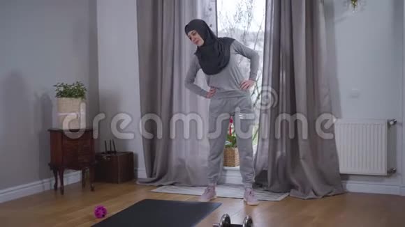 穿着运动服的穆斯林年轻女子站在家里弯腰的画像戴头巾的女强人视频的预览图