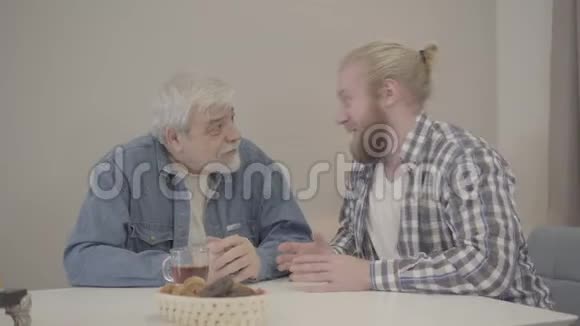 成年白种人的儿子和年长的父亲在家里笑着握手年轻人讲笑话和娱乐视频的预览图