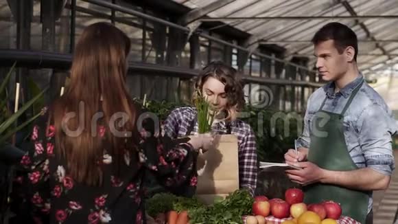 在温室里穿着围裙的快乐的销售伙伴正在向客户销售有机食品女人在给一个视频的预览图