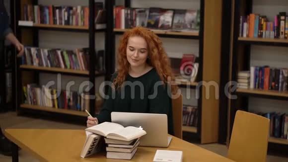 大学图书馆一个长发卷曲的女孩坐在桌子上用笔记本电脑工作的肖像年轻人她视频的预览图