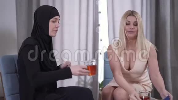 积极的金发白种人女人用糖果对待穆斯林朋友两个来自不同文化的女人喝茶视频的预览图
