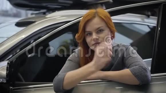 迷人的红发白种人女人坐在汽车上看着镜头微笑幸福车主画像视频的预览图