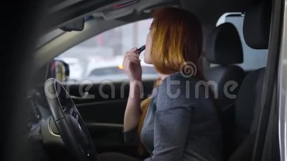 自信的白人红发女人一边涂口红一边坐在车里年轻女子的魅力视频的预览图