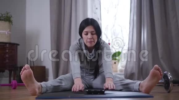 开朗的白种人黑发女人在瑜伽垫和糖果上弯腰向前的肖像微笑的年轻女子视频的预览图