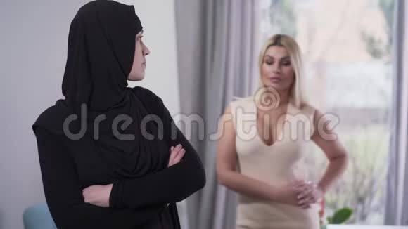 保守的穆斯林女人回头看现代白人女孩穿着坦率的衣服转身离开适度的肖像视频的预览图
