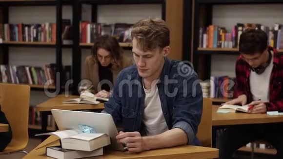 金发白种人坐在大学图书馆里用笔记本电脑工作准备考试然后看着相机视频的预览图