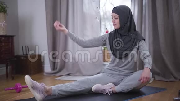 开朗的穆斯林女人炫耀肌肉看着镜头穿着头巾和运动服的年轻微笑女人视频的预览图