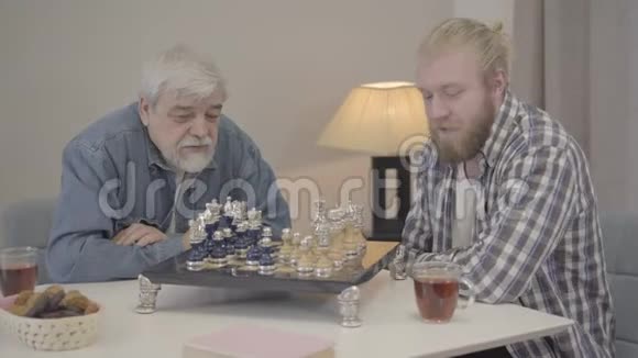 成年的儿子和成熟的父亲在家里像下棋一样喝茶快乐的高加索男人周末的肖像视频的预览图