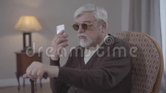 盲人白人老人在室内打电话的肖像灰发男性退休人员手持扶手椅视频的预览图
