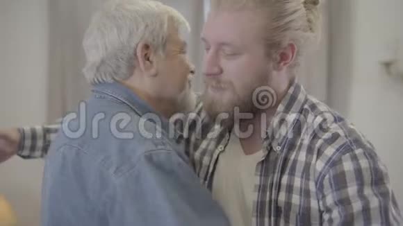 成人白种人男子的特写肖像拥抱年长的白发父亲在室内快乐的儿子和成熟的退休老人微笑视频的预览图