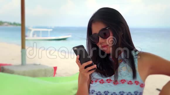 快乐的亚洲女人坐在海滩度假胜地的豆袋里用手机自拍视频的预览图