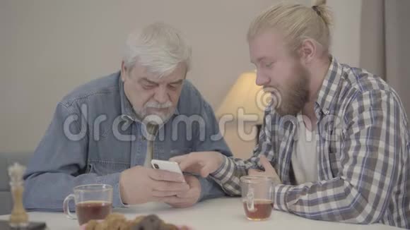 年轻的高加索人教老父亲使用智能手机积极的儿子解释现代技术成熟视频的预览图