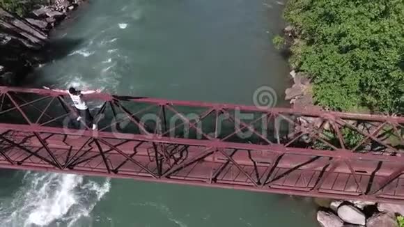 盖伊站起来把他的手臂向旁边的悬崖铁路桥横跨汹涌的河流从空中射击慢动作视频的预览图