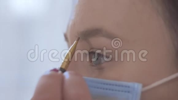 年轻白种人女性戴防护面具化妆的特写侧视女孩使用眉笔视频的预览图