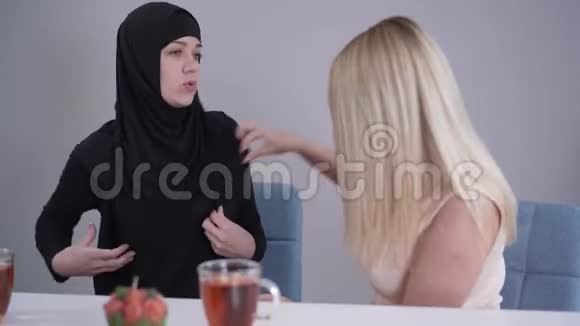 戴头巾的温和穆斯林妇女与金发白种人朋友谈论批评她的服装保守的女士和现代的视频的预览图