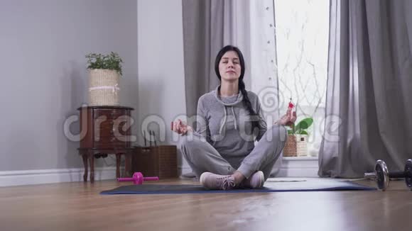 镜头接近自信的黑发白种人女人在家冥想年轻女子双眼坐在瑜伽垫上视频的预览图