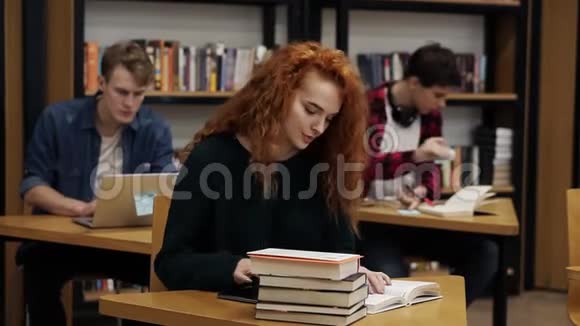 一位年轻的红头卷发女学生正在写论文或准备考试的肖像读一本书视频的预览图