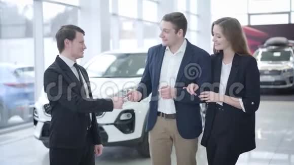 成功的白人商人从经销商那里拿走汽车钥匙并把它们送给快乐的妻子幸福的女人拥抱配偶视频的预览图