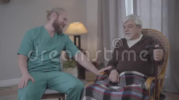 阳性成年白种人穿着护士制服在养老院和成熟的男性退休人员聊天有胡子的年轻人视频的预览图