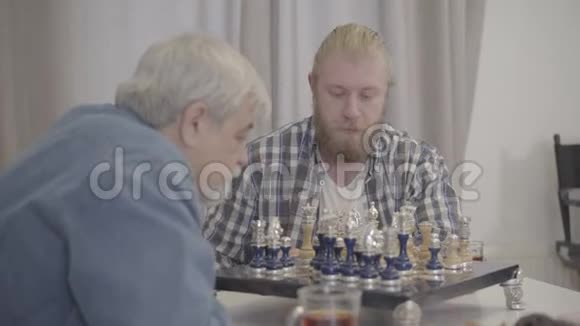 年轻的白种人留胡子男子的肖像集中在与资深父亲的游戏白发苍苍的男性退休者正在下棋视频的预览图