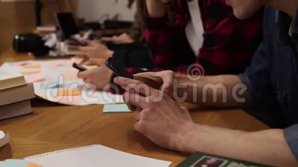 四名大学生在休息和使用智能手机时一起坐在桌子旁的录像发短信视频的预览图