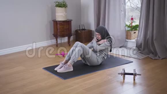 年轻强壮的穆斯林妇女在室内抽压穿着头巾和运动服的苗条运动型女人在家增强肌肉视频的预览图