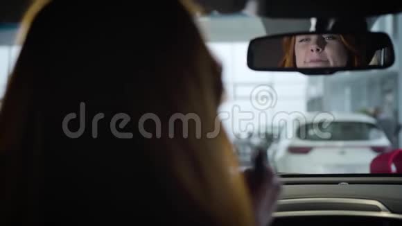 在汽车后视镜里看到漂亮的白人女人涂口红自信的女车主坐着视频的预览图