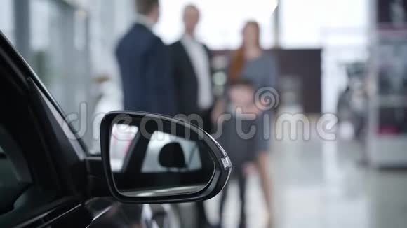 汽车后视镜的特写模糊的人在后台交谈高加索经销商咨询家庭视频的预览图